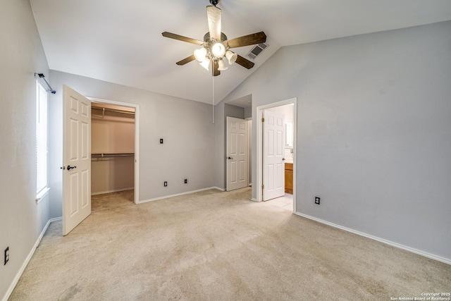 unfurnished bedroom with lofted ceiling, light carpet, visible vents, baseboards, and a walk in closet