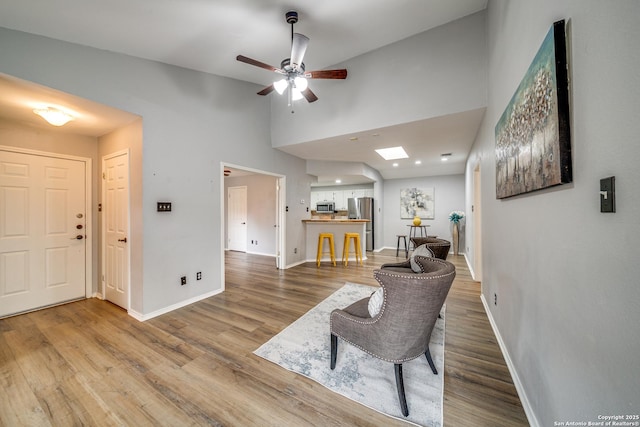 living area featuring a skylight, ceiling fan, baseboards, and wood finished floors