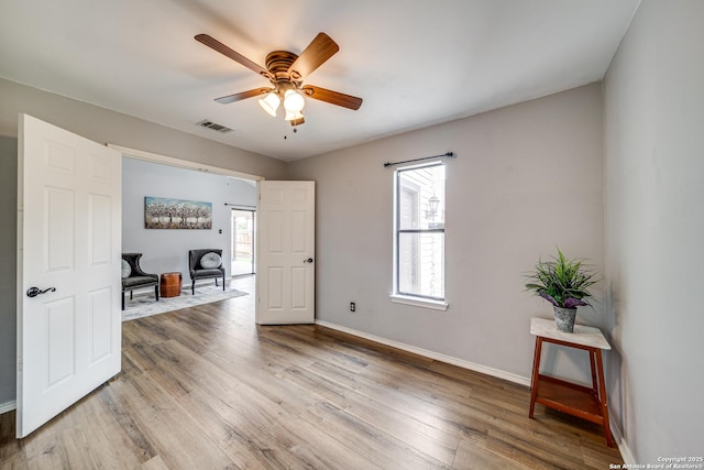 interior space with a ceiling fan, baseboards, visible vents, and wood finished floors