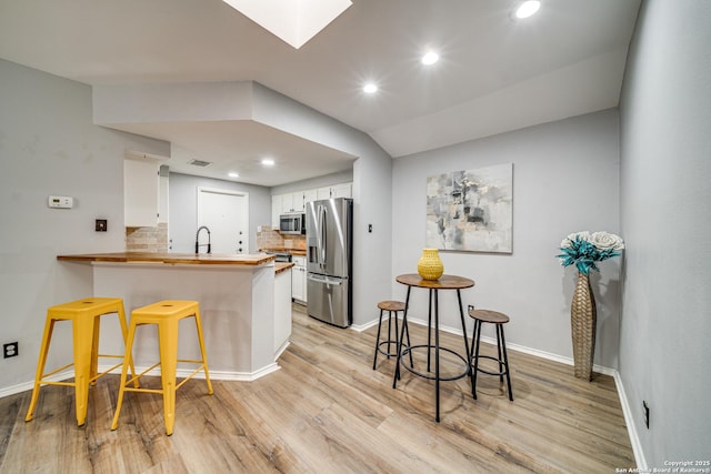 kitchen with light wood-style flooring, appliances with stainless steel finishes, a breakfast bar, a peninsula, and white cabinetry