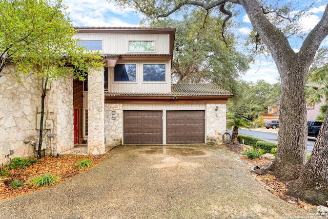 view of front of house with driveway, stone siding, a tile roof, and a garage