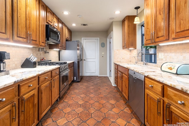 kitchen featuring light stone counters, stainless steel appliances, a sink, brown cabinetry, and decorative light fixtures