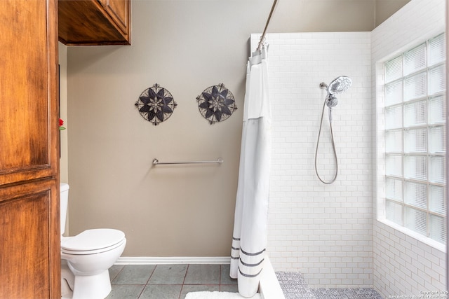 bathroom with tile patterned flooring, tiled shower, toilet, and baseboards