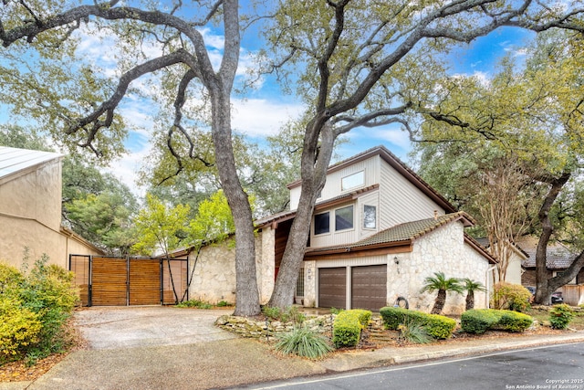 mid-century home with driveway, stone siding, a tile roof, an attached garage, and fence