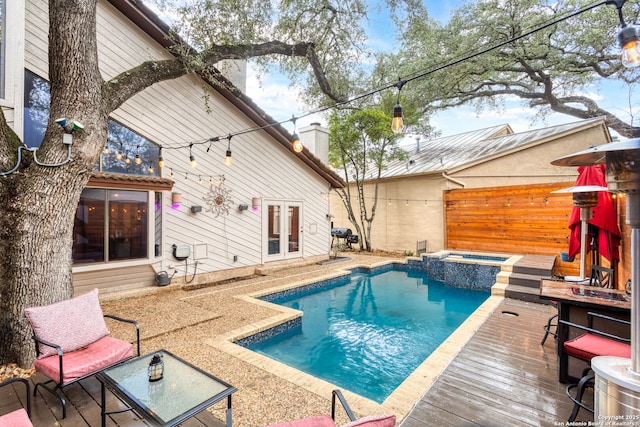 view of swimming pool featuring a deck, fence, and a pool with connected hot tub