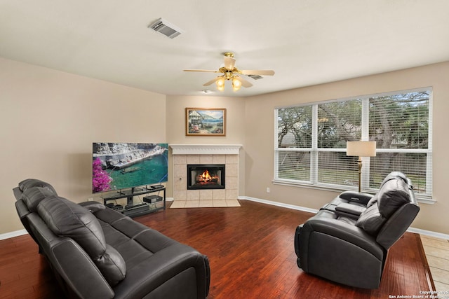 living area with visible vents, ceiling fan, wood finished floors, a tile fireplace, and baseboards