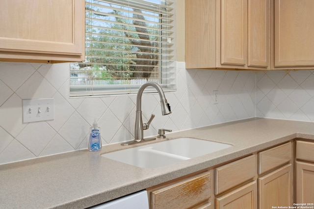 kitchen with light countertops, a sink, backsplash, and light brown cabinetry