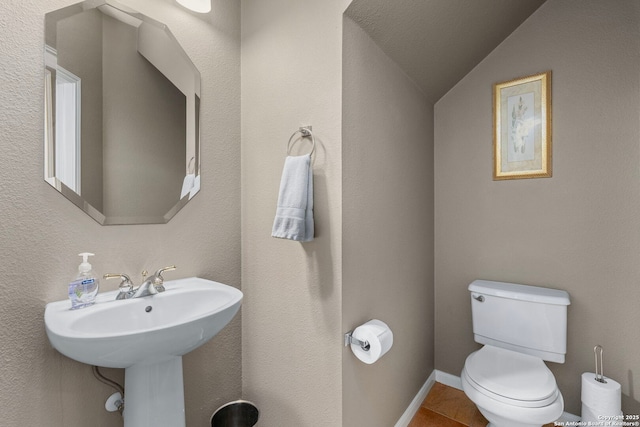 bathroom with lofted ceiling, baseboards, tile patterned flooring, and toilet