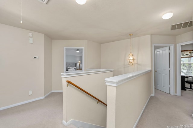 hall featuring visible vents, baseboards, an upstairs landing, and light colored carpet