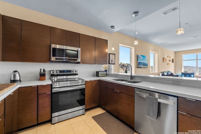 kitchen featuring appliances with stainless steel finishes, light countertops, a sink, and decorative light fixtures