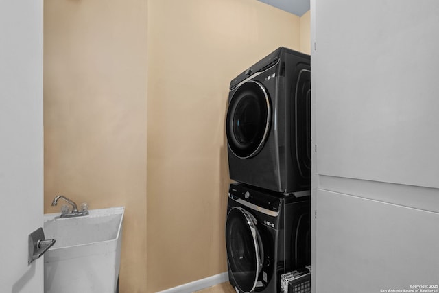 clothes washing area featuring stacked washer and dryer, baseboards, laundry area, and a sink