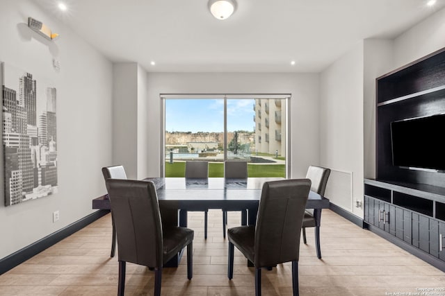 dining room featuring light wood-style flooring, a view of city, baseboards, and recessed lighting