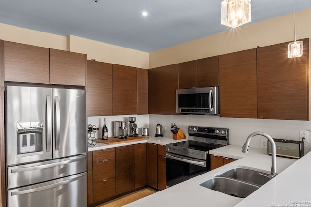 kitchen featuring modern cabinets, stainless steel appliances, light countertops, pendant lighting, and a sink