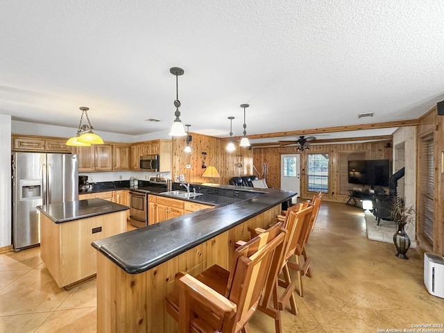 kitchen with dark countertops, appliances with stainless steel finishes, open floor plan, pendant lighting, and a sink