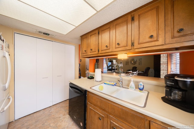 kitchen featuring black dishwasher, light countertops, brown cabinetry, freestanding refrigerator, and a sink