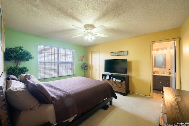 bedroom with a ceiling fan, light carpet, a textured ceiling, and ensuite bath