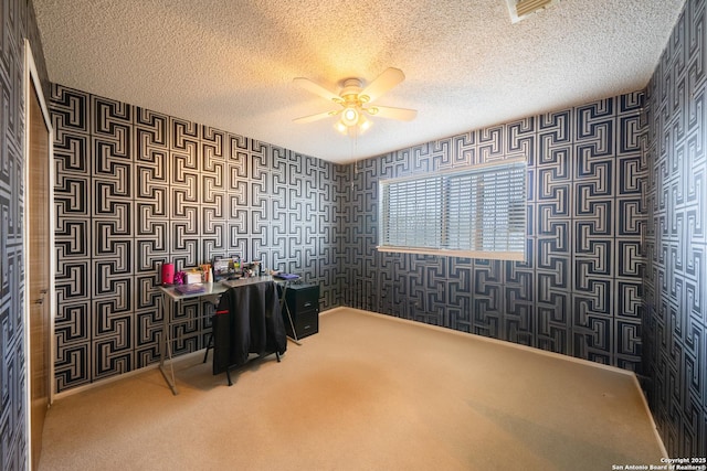 carpeted home office featuring a textured ceiling, ceiling fan, visible vents, and wallpapered walls