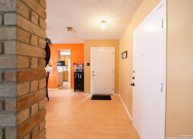 hall featuring light wood-type flooring, visible vents, baseboards, and a textured ceiling