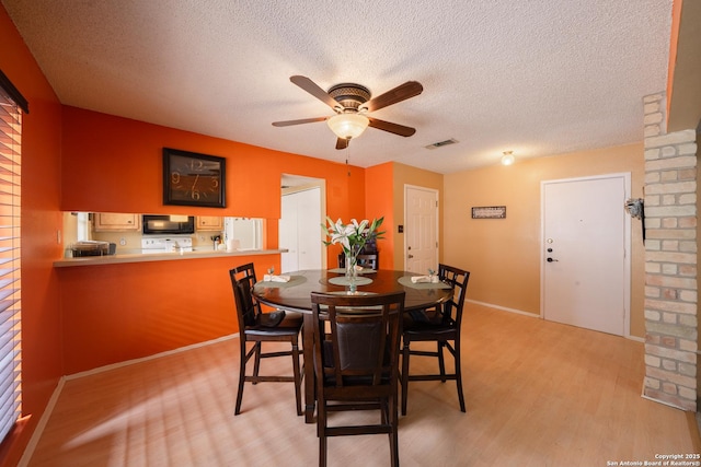 dining room featuring a ceiling fan, light wood-type flooring, visible vents, and a textured ceiling