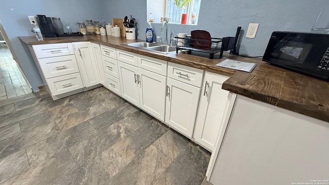 kitchen featuring black microwave, butcher block counters, a sink, and white cabinetry