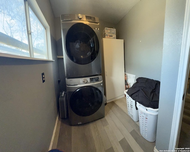 clothes washing area featuring stacked washer / dryer, laundry area, and light wood finished floors