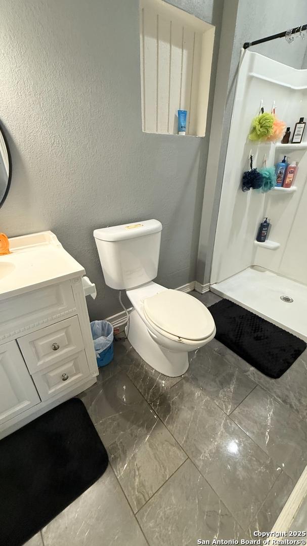 bathroom featuring a stall shower, a textured wall, vanity, and toilet