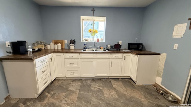 kitchen featuring dark countertops, decorative light fixtures, a sink, and white cabinetry