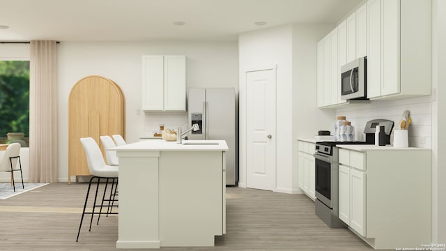 kitchen with a breakfast bar area, stainless steel appliances, light countertops, white cabinetry, and an island with sink