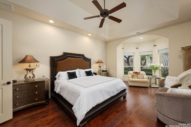 bedroom with dark wood-style floors, visible vents, arched walkways, and a raised ceiling