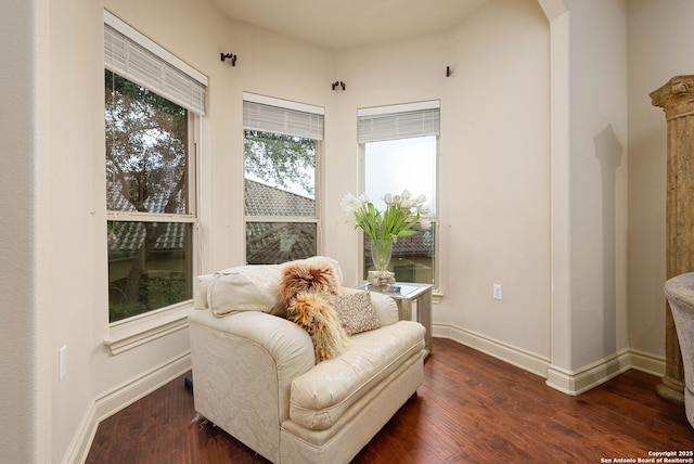 living area featuring arched walkways, dark wood finished floors, and baseboards