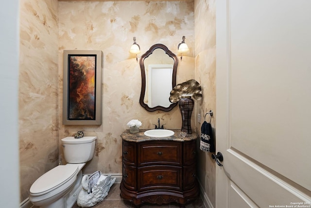 half bath with baseboards, vanity, toilet, and wallpapered walls