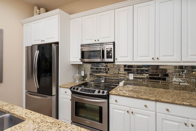 kitchen with stainless steel appliances, white cabinetry, backsplash, and light stone countertops