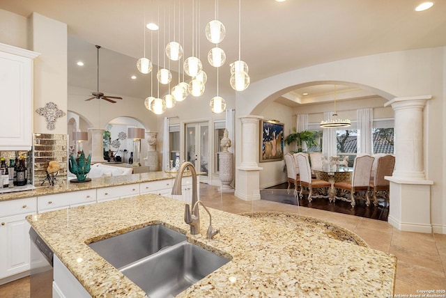 kitchen with a sink, hanging light fixtures, decorative columns, and light stone countertops