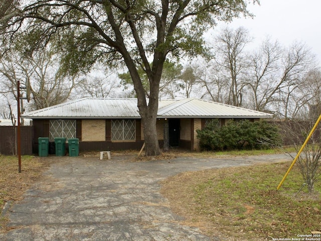 ranch-style home featuring aphalt driveway, brick siding, and metal roof