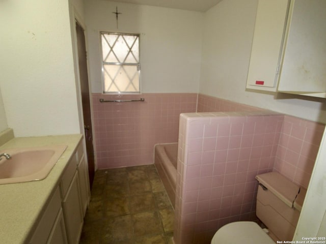 bathroom featuring wainscoting, toilet, a tub, vanity, and tile walls