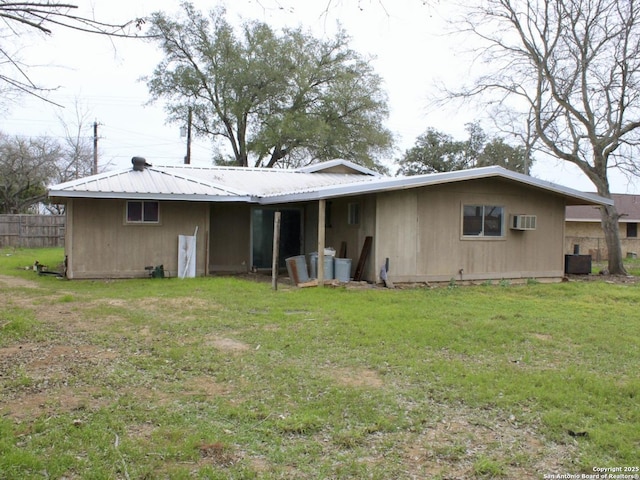 rear view of house featuring a wall unit AC, fence, metal roof, and a yard