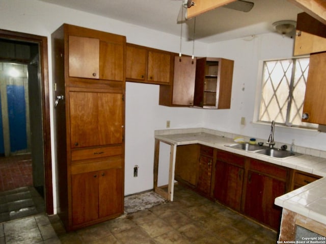 kitchen with ceiling fan, brown cabinetry, a sink, and tile counters