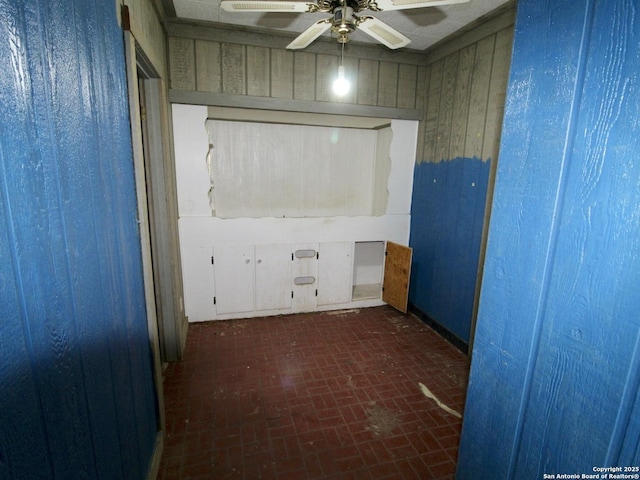 unfurnished room with wood walls, brick floor, and a ceiling fan