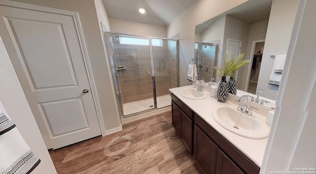 full bathroom with a stall shower, double vanity, a sink, and wood finished floors