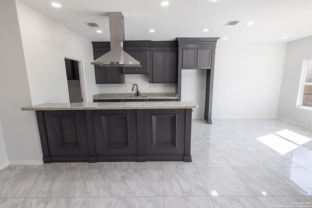 kitchen featuring light stone countertops, visible vents, island range hood, and a sink