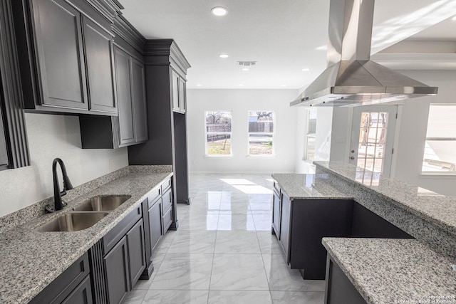 kitchen with marble finish floor, a healthy amount of sunlight, a sink, island range hood, and light stone countertops