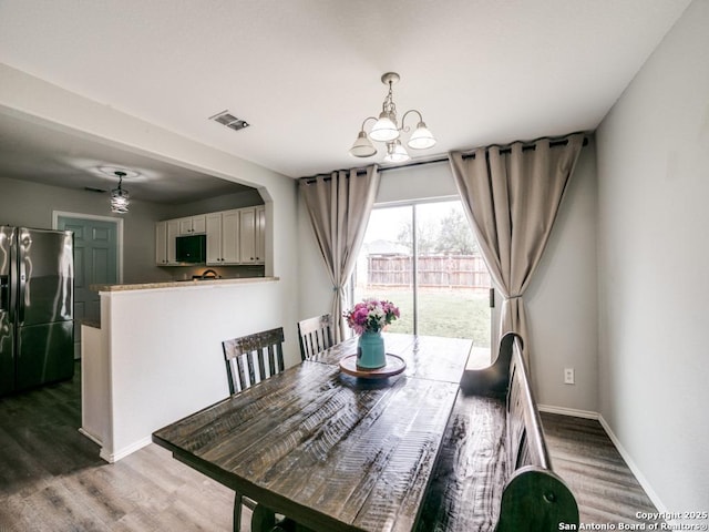 dining room with baseboards, visible vents, a chandelier, and wood finished floors