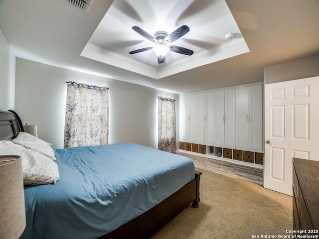 bedroom with a ceiling fan, visible vents, a tray ceiling, and crown molding