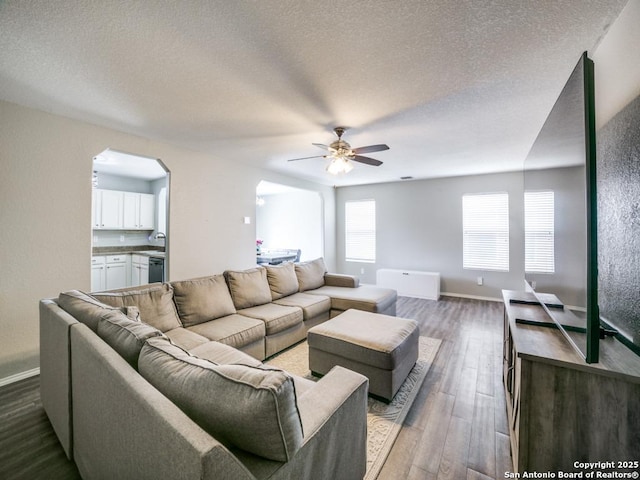 living area with a ceiling fan, a textured ceiling, baseboards, and dark wood-type flooring