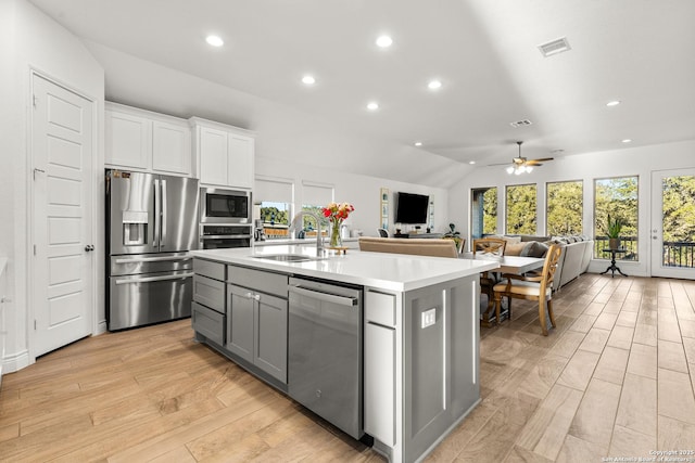 kitchen featuring a kitchen island with sink, white cabinetry, open floor plan, light countertops, and appliances with stainless steel finishes