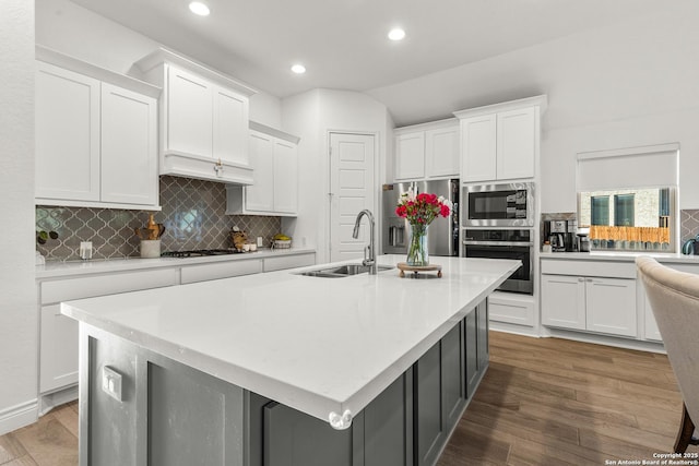 kitchen with light countertops, appliances with stainless steel finishes, a center island with sink, and white cabinetry