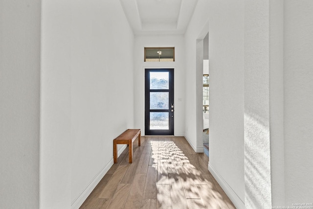 doorway to outside featuring baseboards, a raised ceiling, and light wood-style floors