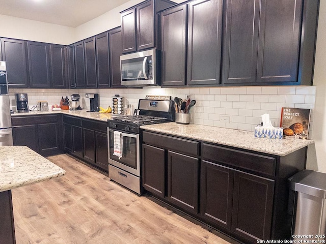 kitchen featuring stainless steel appliances, light wood finished floors, backsplash, and light stone countertops