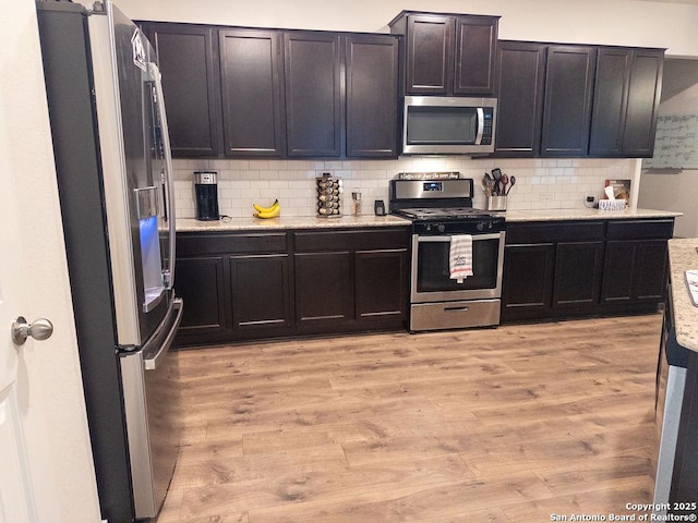 kitchen featuring stainless steel appliances, light stone counters, backsplash, and light wood-style flooring