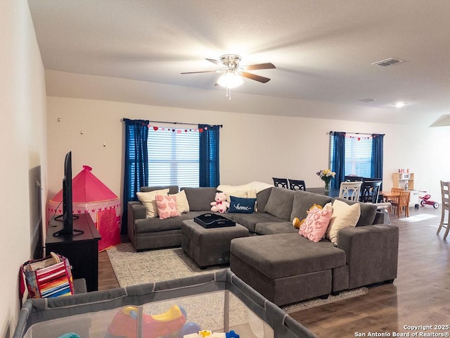 living area with a healthy amount of sunlight, ceiling fan, visible vents, and wood finished floors